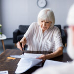 Do seniors over 70 need to do federal tax returns every year? - Selective focus of senior woman holding pen and papers near credit card and husband at home