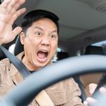 A man is yelling in a car is driving a car and looking at his cell phone. He is surprised and excited. Concept of distraction while driving and the potential danger it poses.